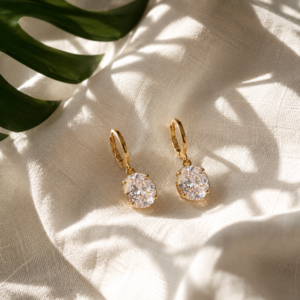 Gold oval crystal drop earrings with sparkling stones displayed on a white textured block