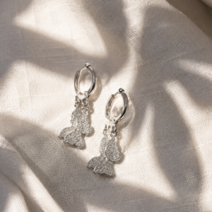 Silver butterfly hoop earrings with textured charms displayed on a white stone block