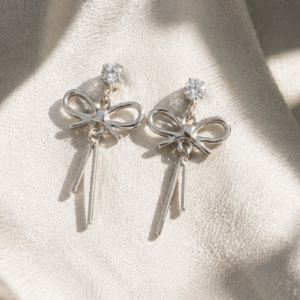 Minimal silver bow drop earrings with crystal studs held on fingertips